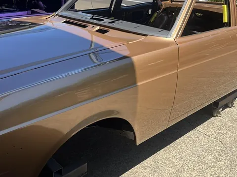 Bronze classic sedan on a workshop dolly, freshly painted with the interior stripped and ready for assembly